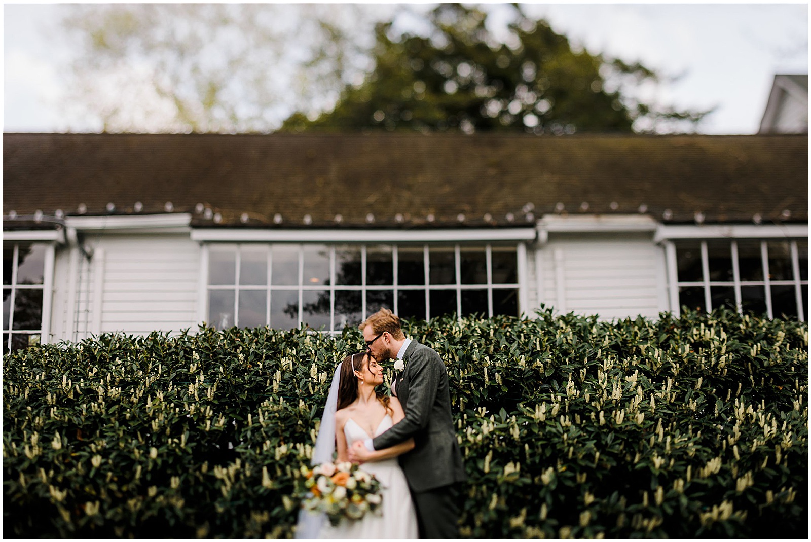 A bride and groom pose in front of a flowering bush at a New Jersey wedding venue.