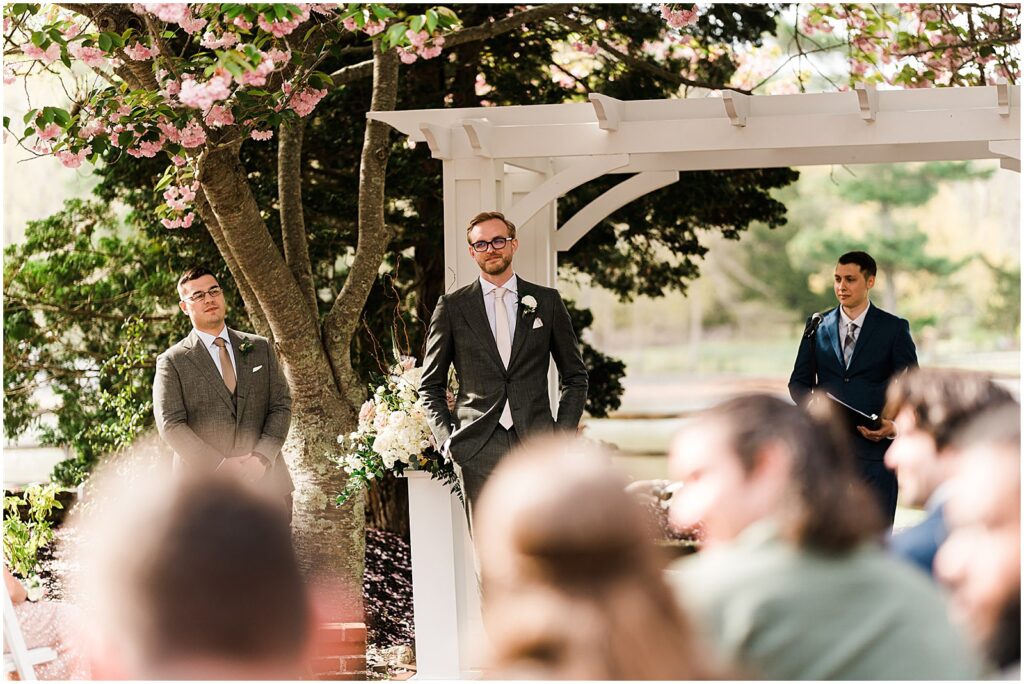 A groom tears up when he sees a bride coming down the aisle at a courtyard wedding ceremony.