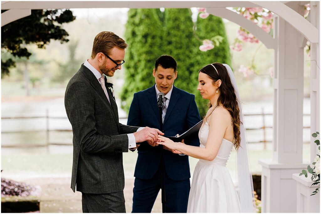 A groom puts a ring on a bride's finger during a spring wedding ceremony.