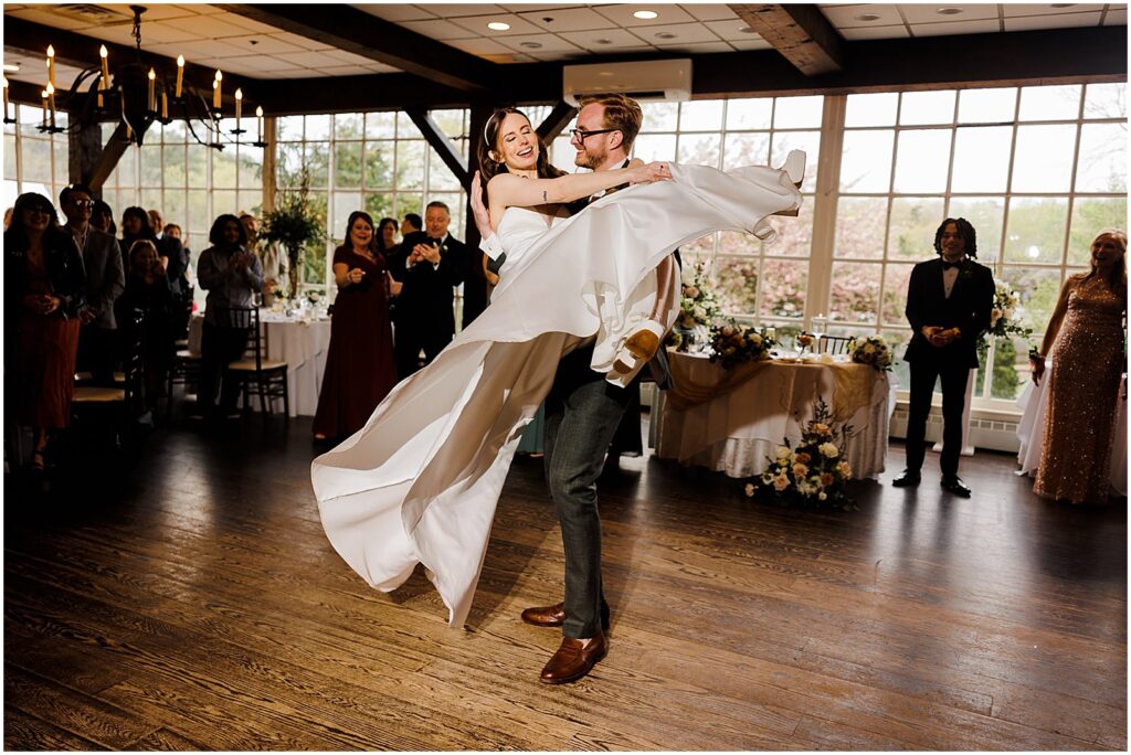 A bride and groom laugh as they dance together.