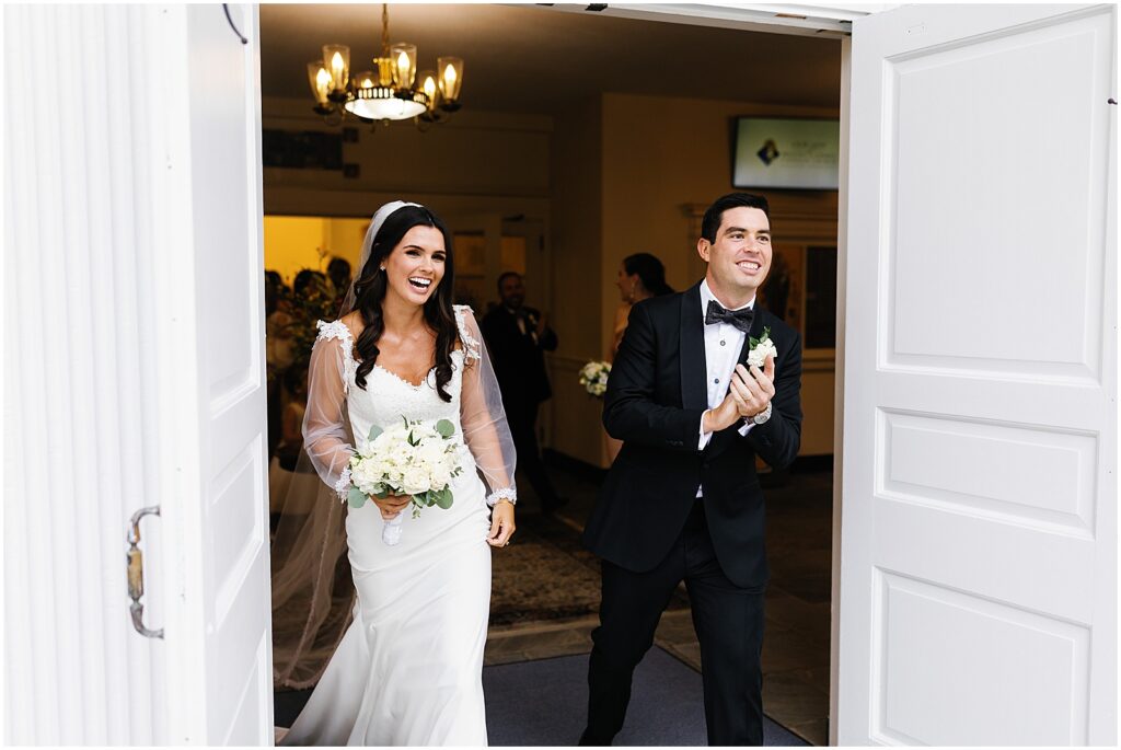 A bride and groom laugh and walk through church doors.