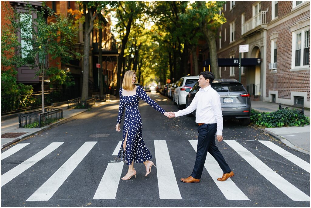 A woman leads a man by the hand across a Brooklyn street during their engagement photo session.