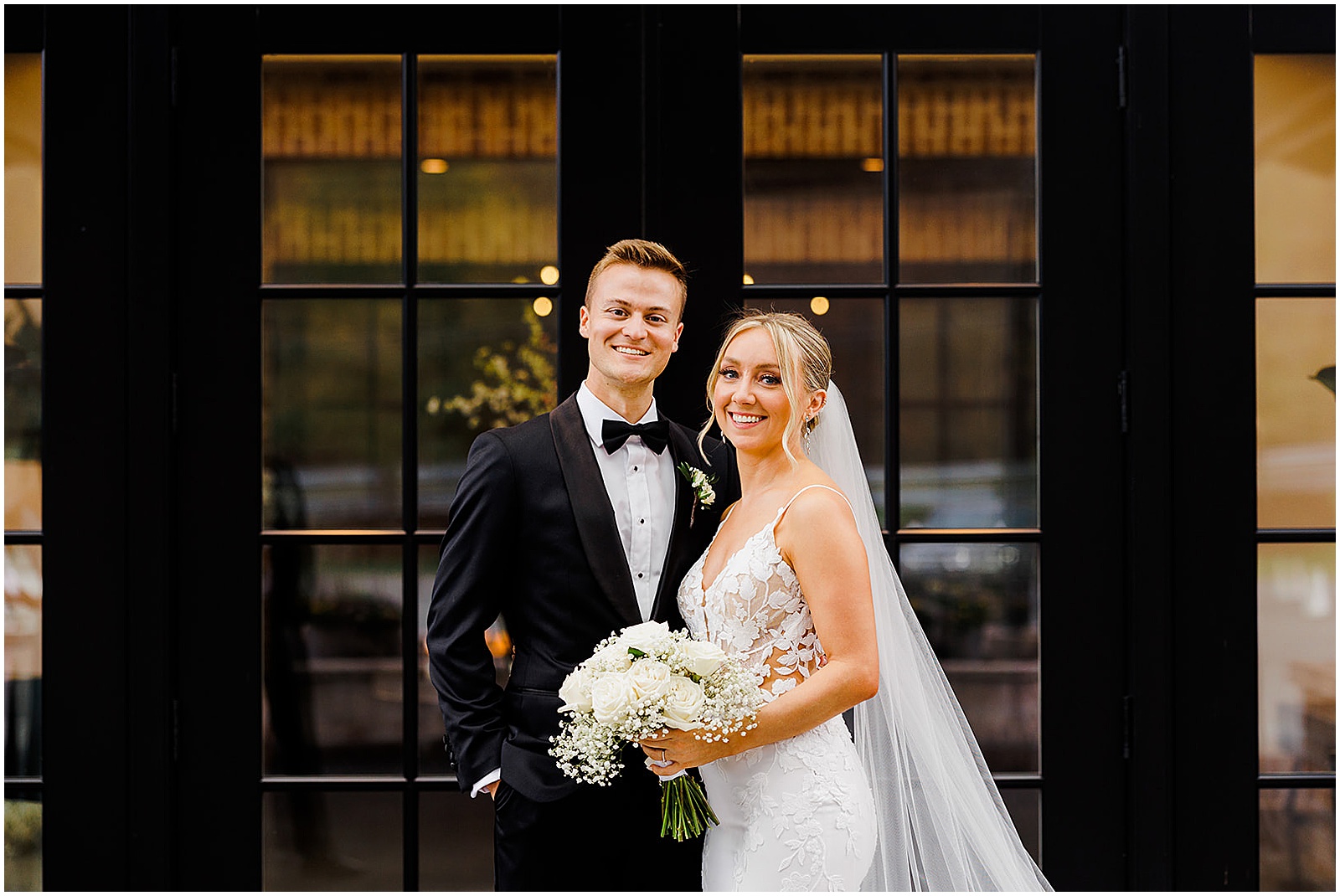 A bride and groom pose in front of glass doors at their Perona Farms wedding.