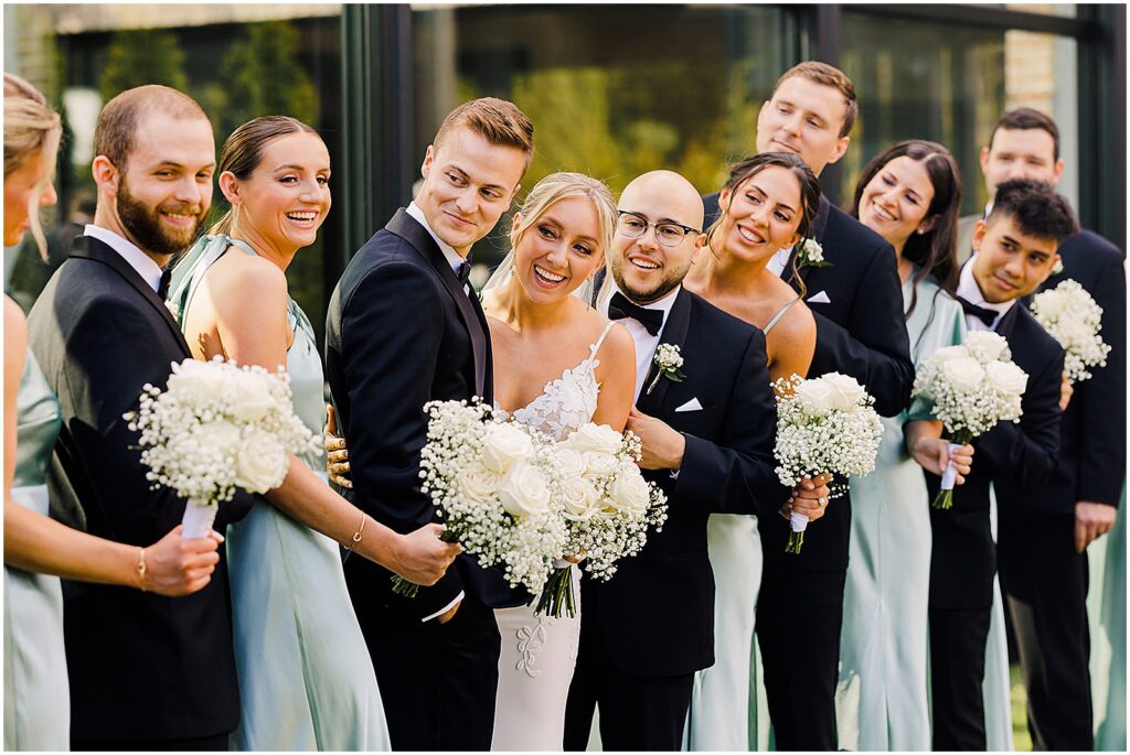 A bride and groom stand in a line with their wedding party laughing.