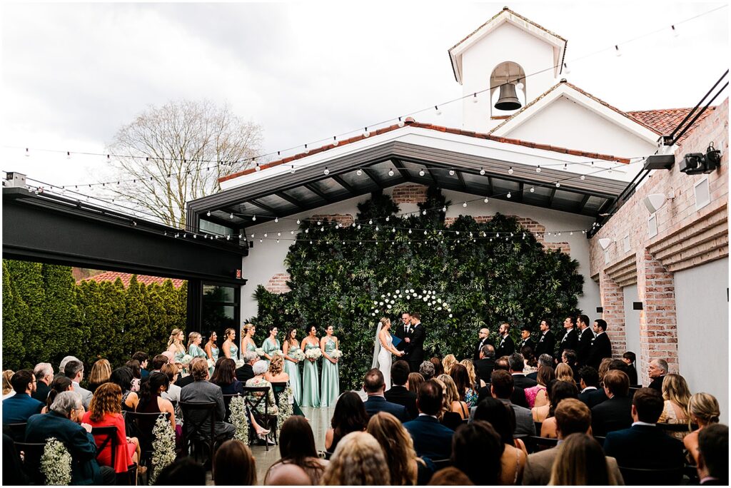 Guests sit in a courtyard to watch a Perona Farms wedding ceremony on a cloudy day.