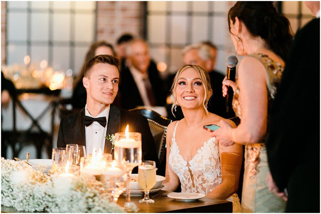 A bride and groom smile during a maid of honor toast at a New Jersey wedding reception.