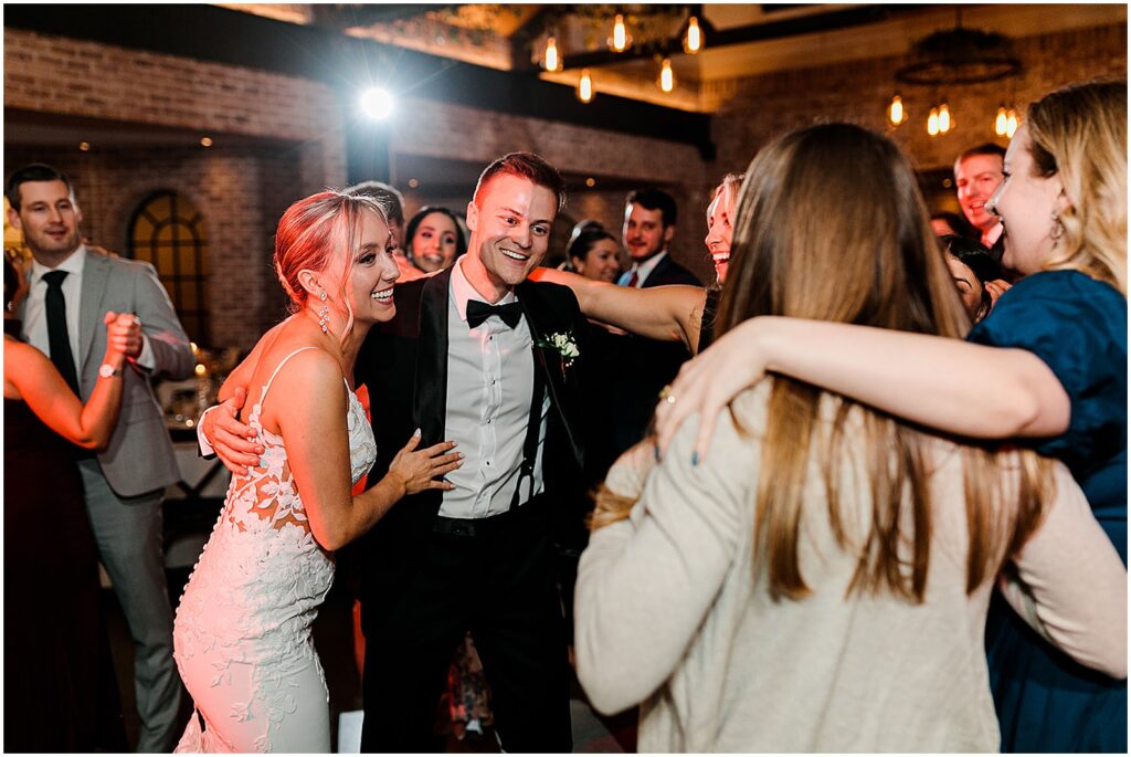 A bride and groom laugh with friends on the dance floor.