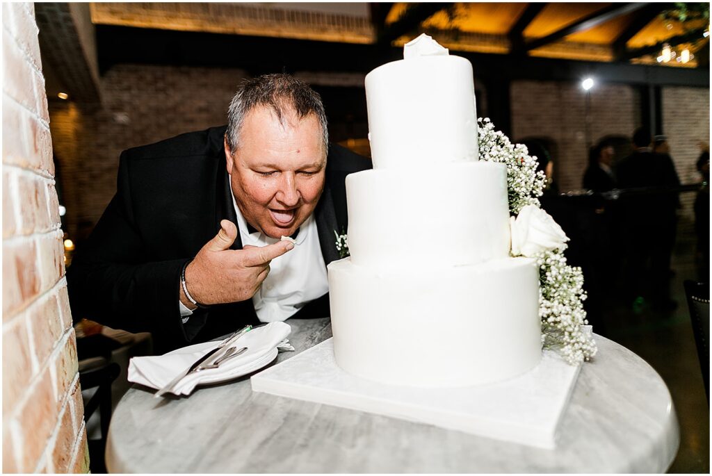 A family member leans over a wedding cake with icing on his finger.
