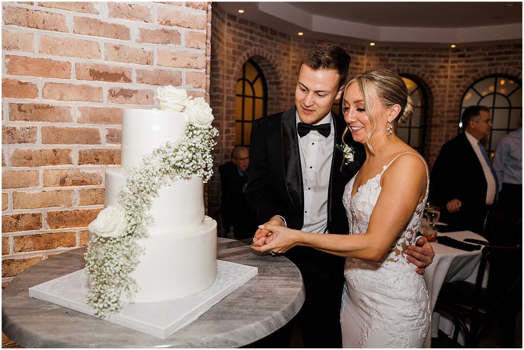A bride and groom cut a tiered wedding cake at their Perona Farms wedding.