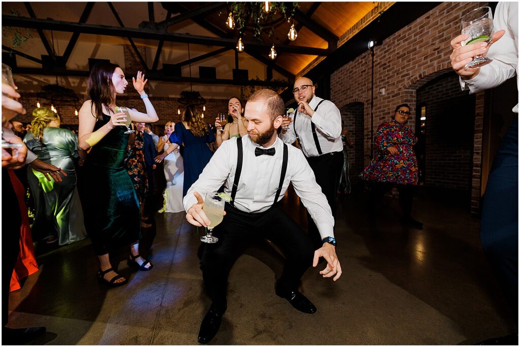 A groomsman dances with a drink in his hand.