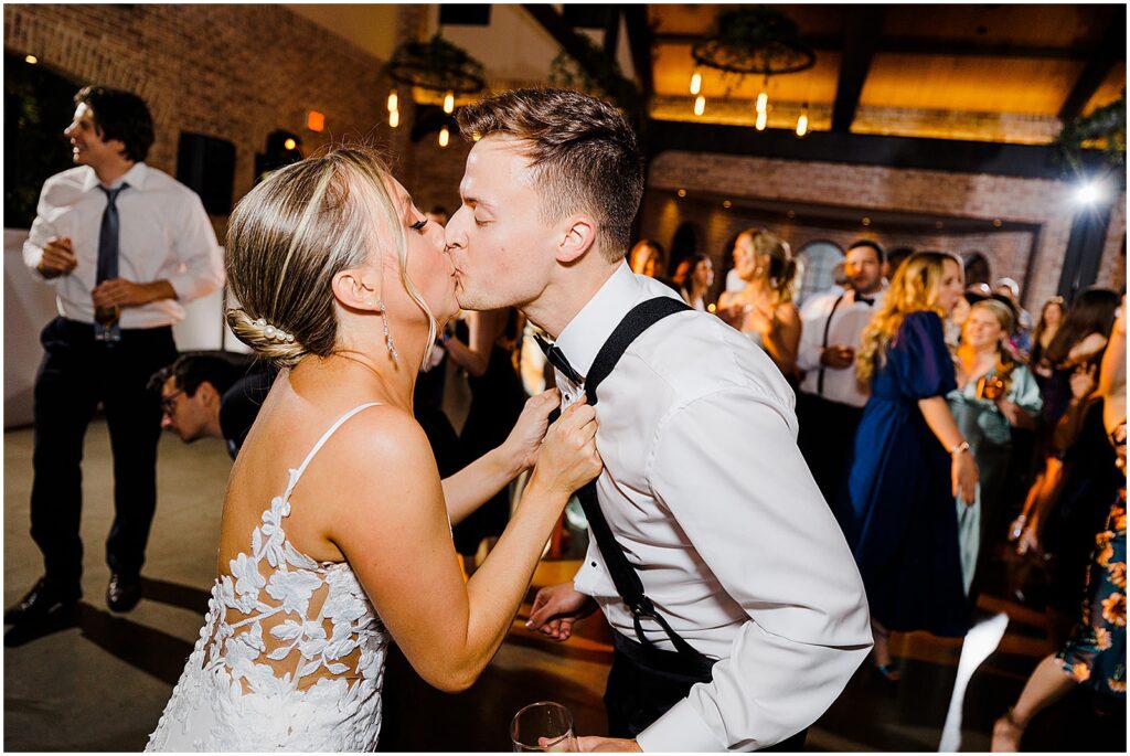 A bride grabs a groom by the suspenders and kisses him.