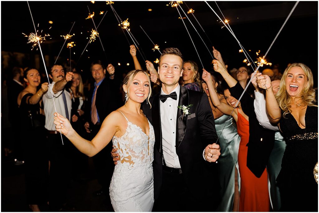A bride and groom pose with wedding guests holding sparklers.