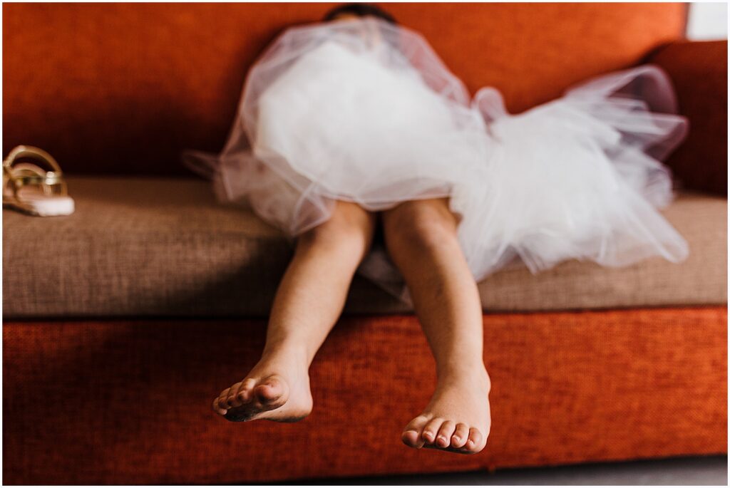 A flower girl sits dangling her legs from a couch.