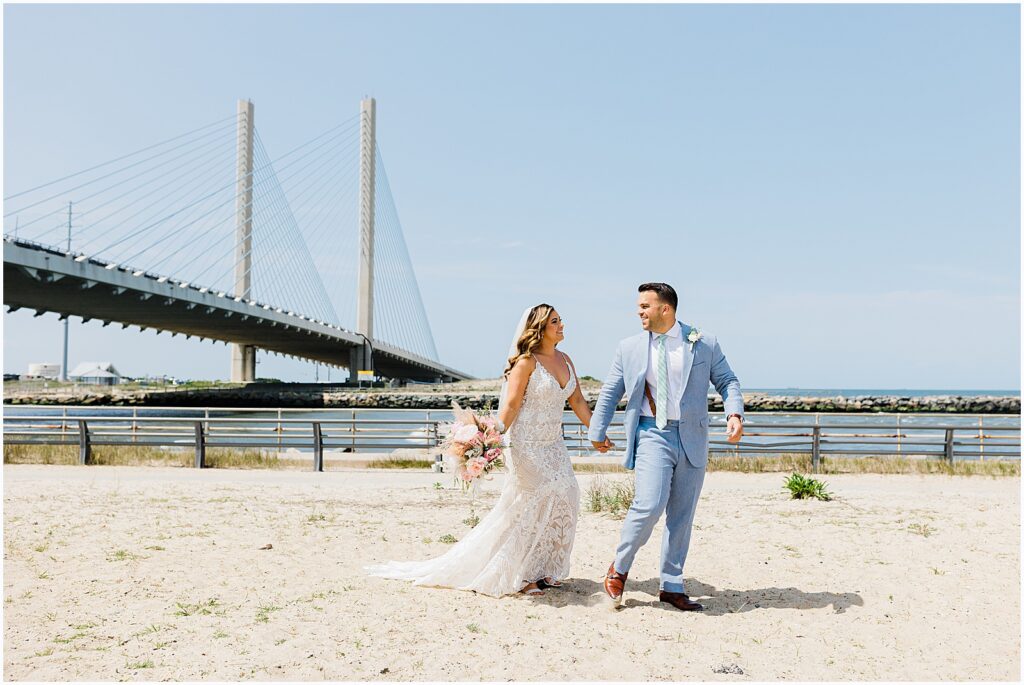 A bride and groom hold hands and walk along Dewey Beach.