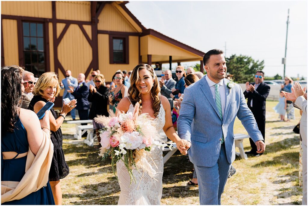 A bride and groom smile as they walk their recessional at a beach wedding venue in Delaware.