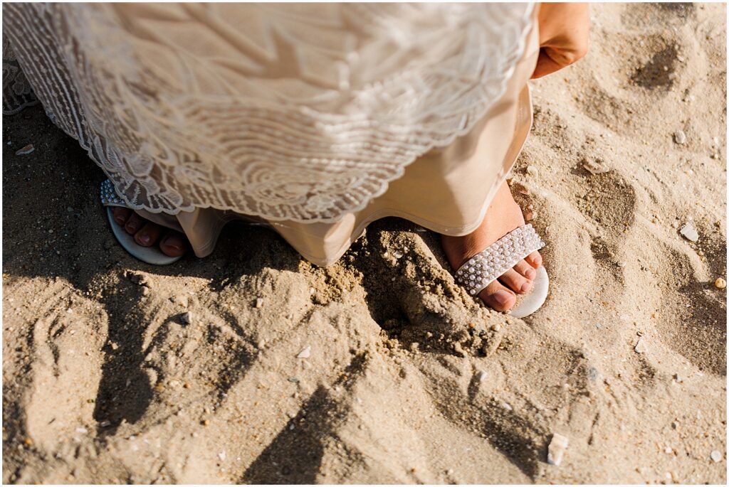 A bride walks on a beach in white wedding sandals.