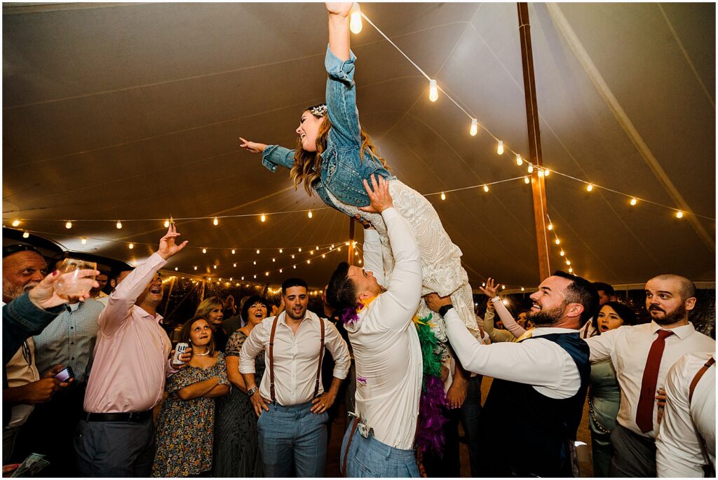 Wedding guests lift a bride above their heads on the dance floor.