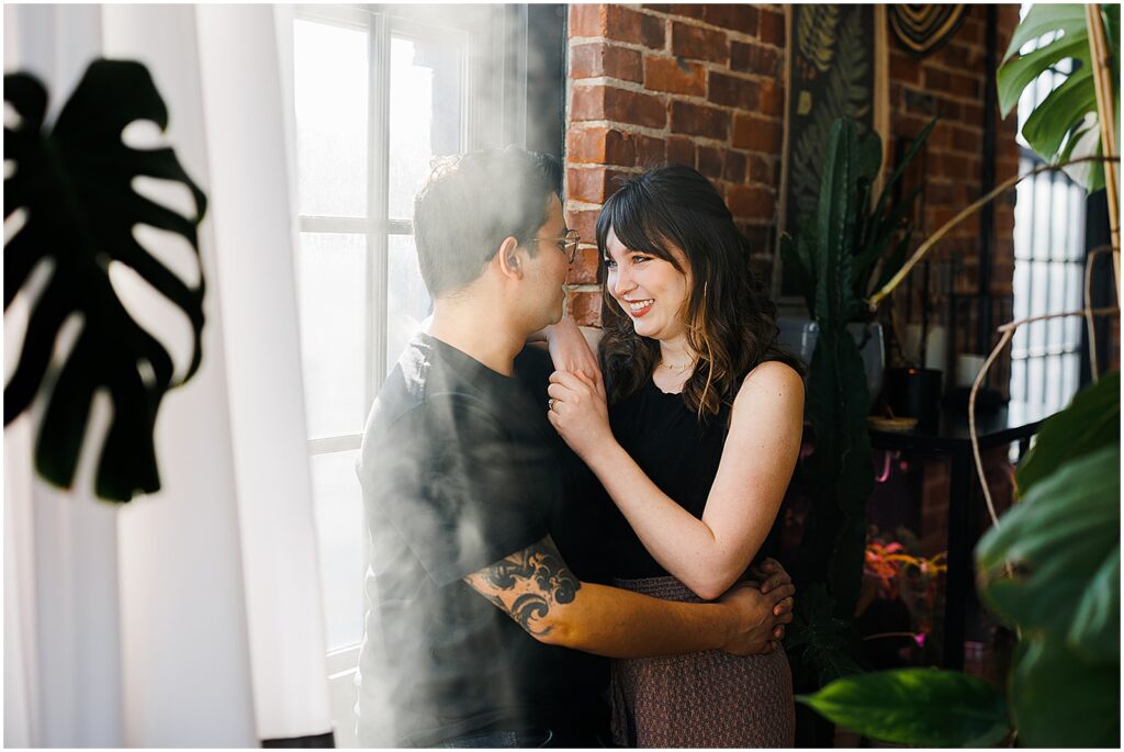 A man and woman pose for anniversary photos beside a window in a Phoenixville apartment.