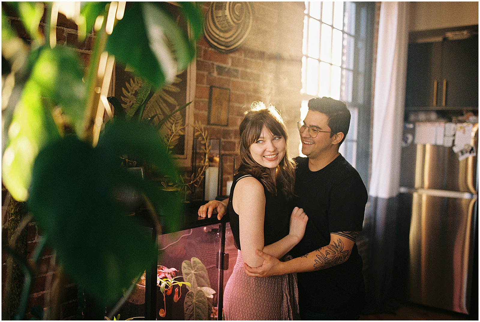A woman leans on her husband and laughs in a sunny living room.