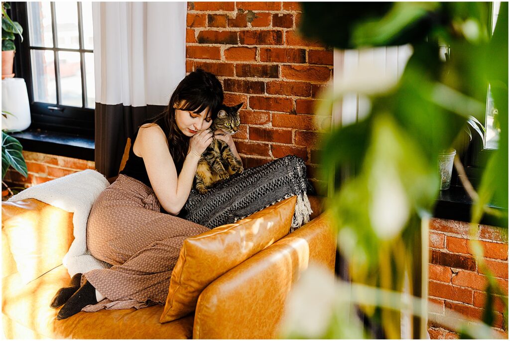 A woman cuddles her cat on a leather couch during a lifestyle photography session.