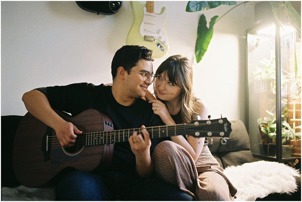 A woman leans on her husband while he plays his guitar on film photography.