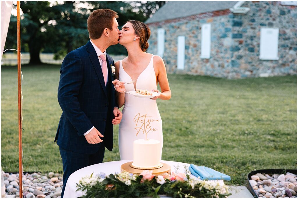 A bride and groom kiss beside their wedding cake.