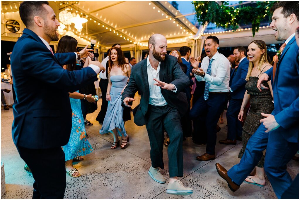 A wedding guest dances while groomsmen cheer.