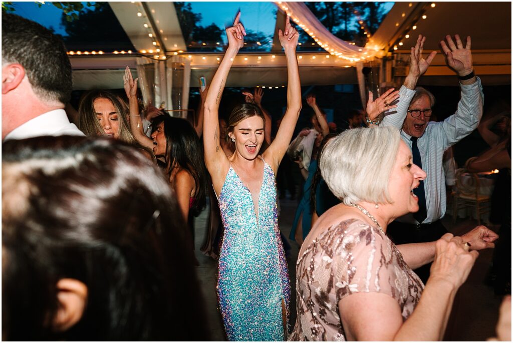 A bride in a sequin reception dress raises her arms on the dance floor at Bellevue Hall.