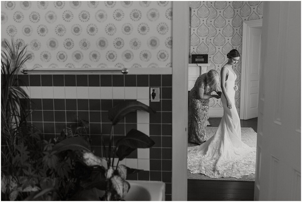 A bride's mother zips up her dress in a suite at Bellevue Hall.