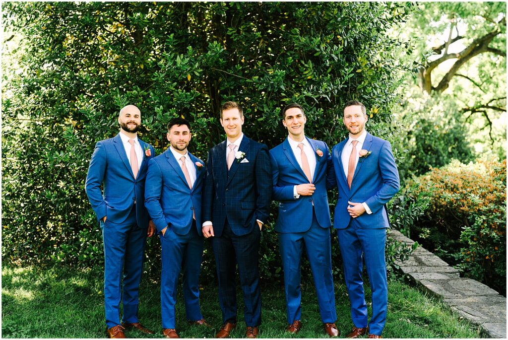 A groom poses with groomsmen in blue suits.