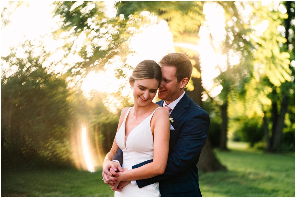 A bride smiles and leans against a groom in a golden hour wedding photo.