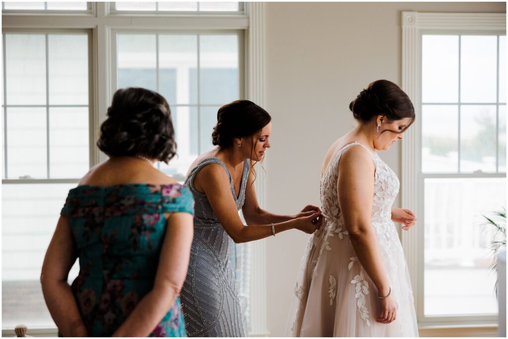 A bridesmaid zips up a bride's wedding dress in a sunny getting ready suite.