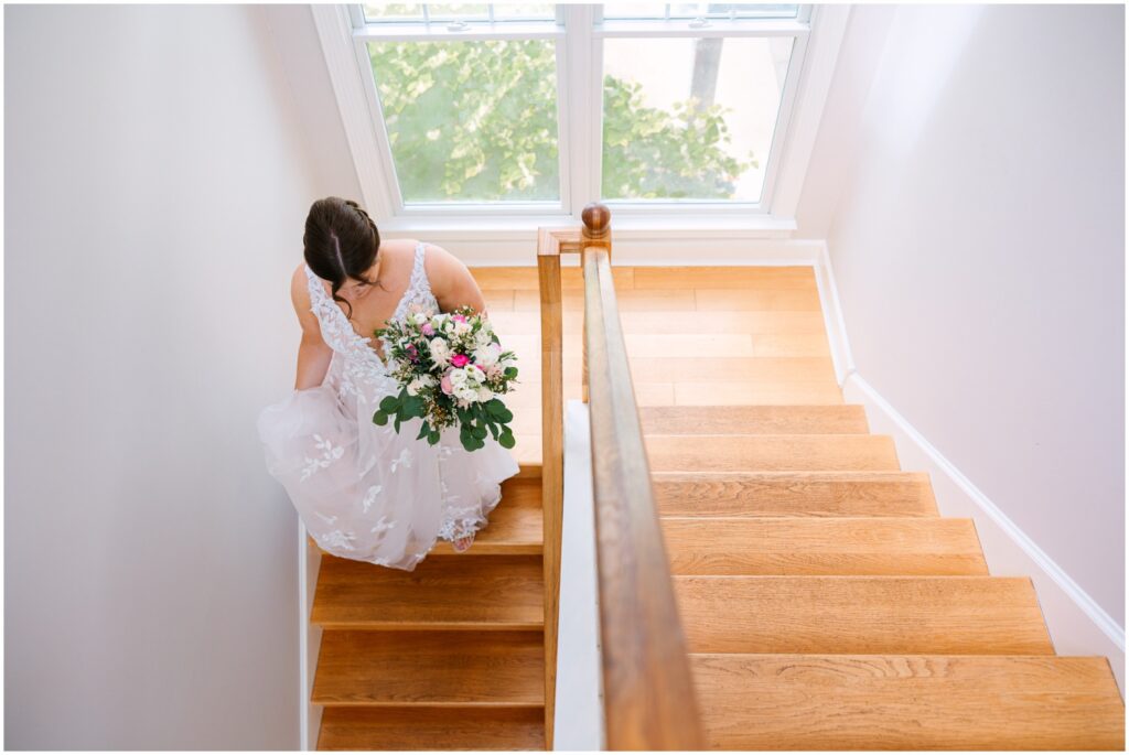 A bride walks down a sunny staircase in a Delaware wedding venue.