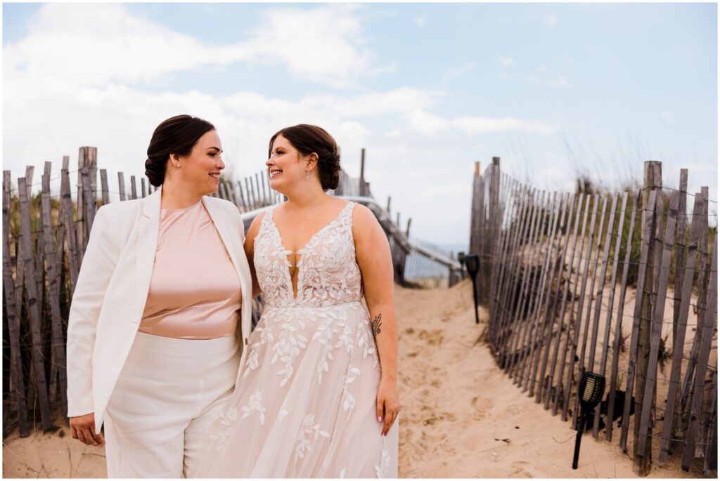 Two brides walk down a sandy path at Bethany Beach.