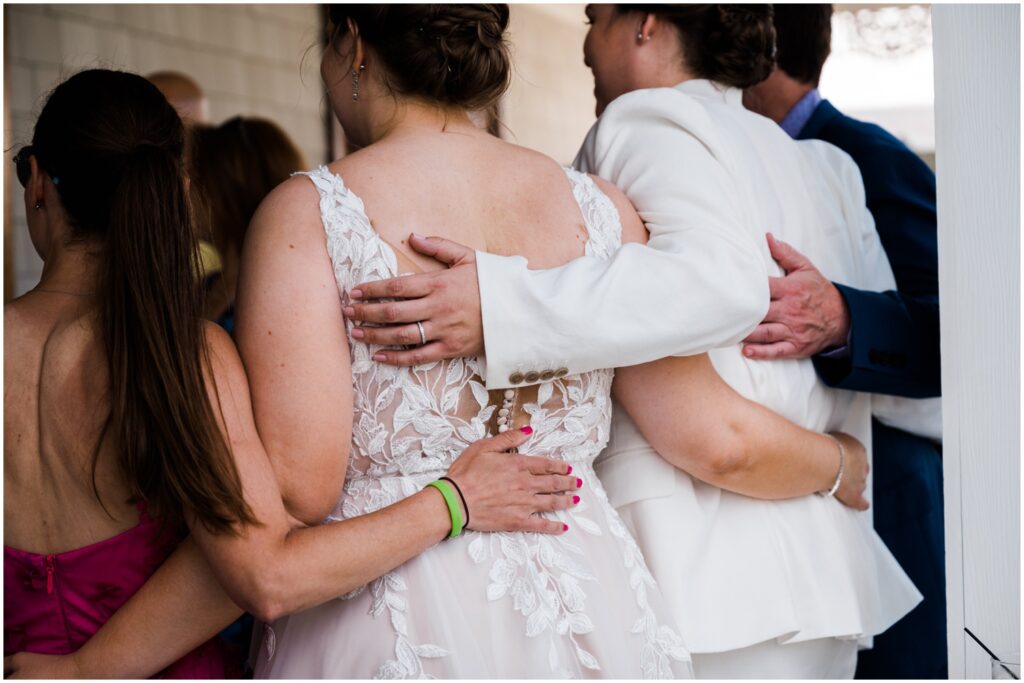 Two brides stand with their arms around wedding guests.
