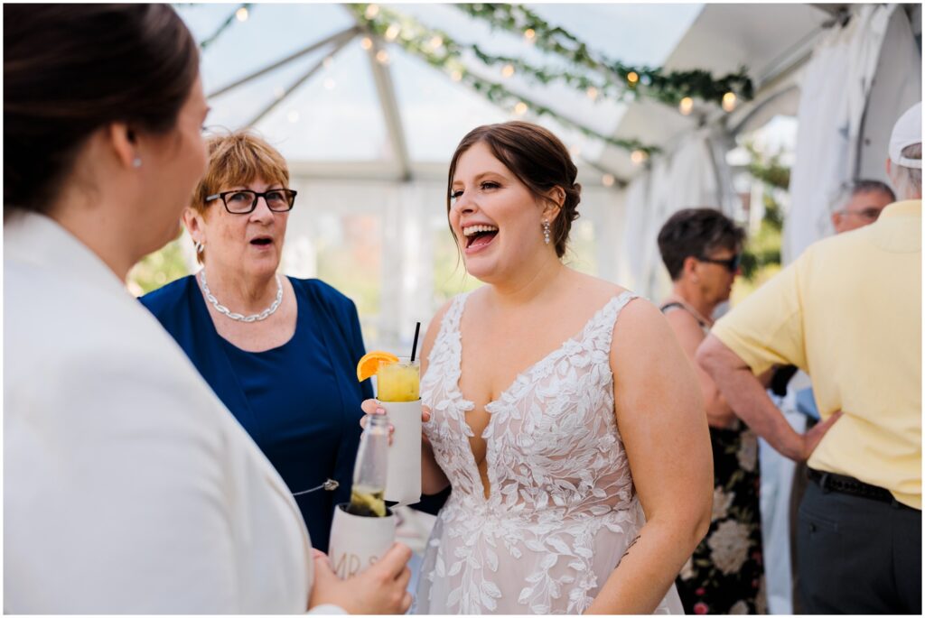 A bride holds a cocktail and laughs with wedding guests.