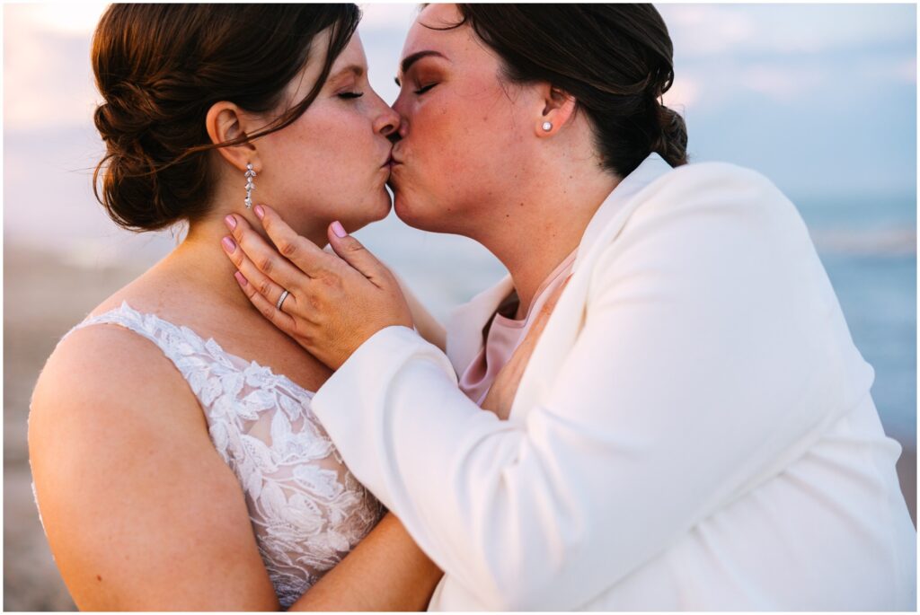 Two brides kiss at sunset on the beach.