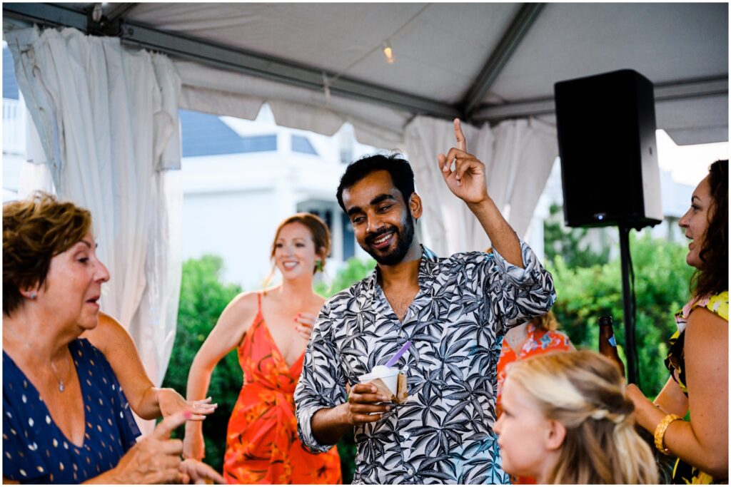 Wedding guests dance in a circle under a white tent.