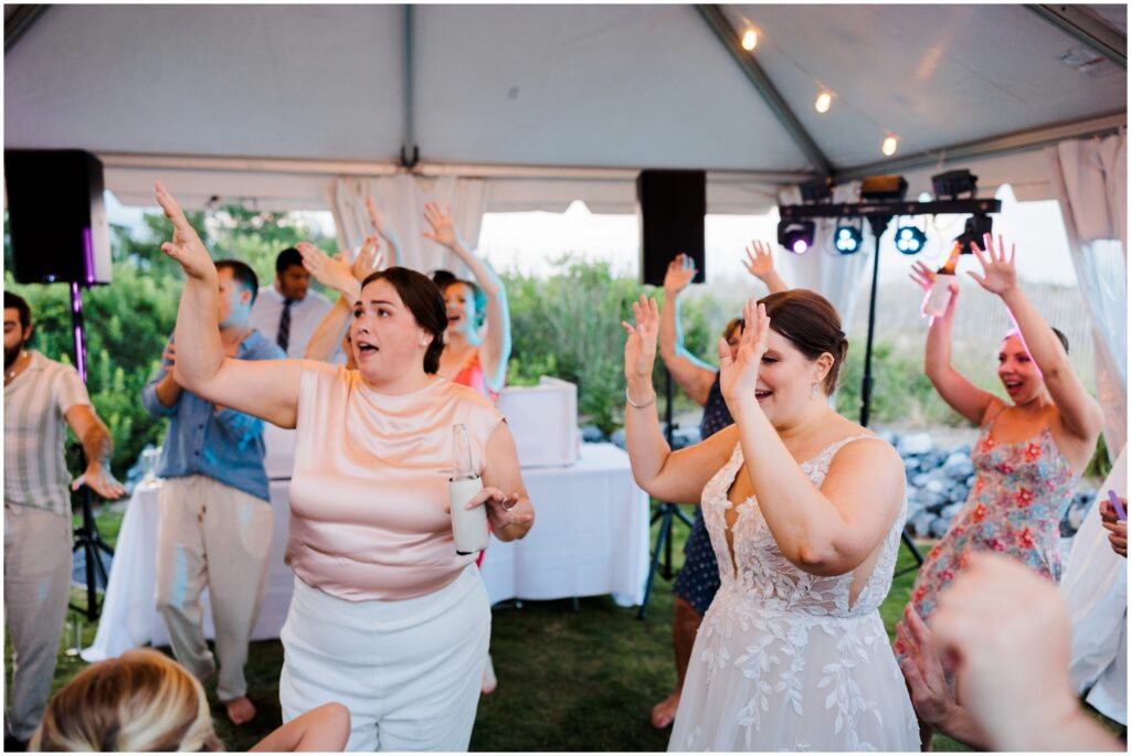 Two brides throw their arms in the air as they dance with guests.