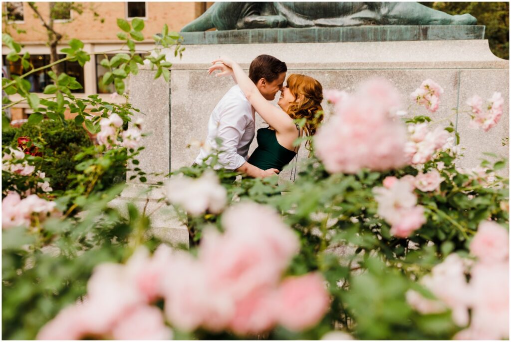 A man and woman nuzzle behind a rose bush in a New Jersey engagement photo.