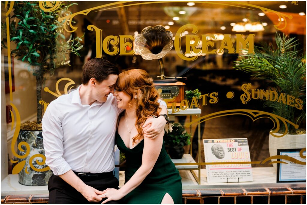A man and woman lean against a diner window during an engagement session.