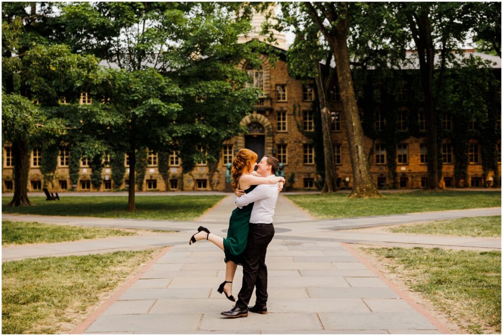 A man picks up a woman with a Princeton university building in the background.
