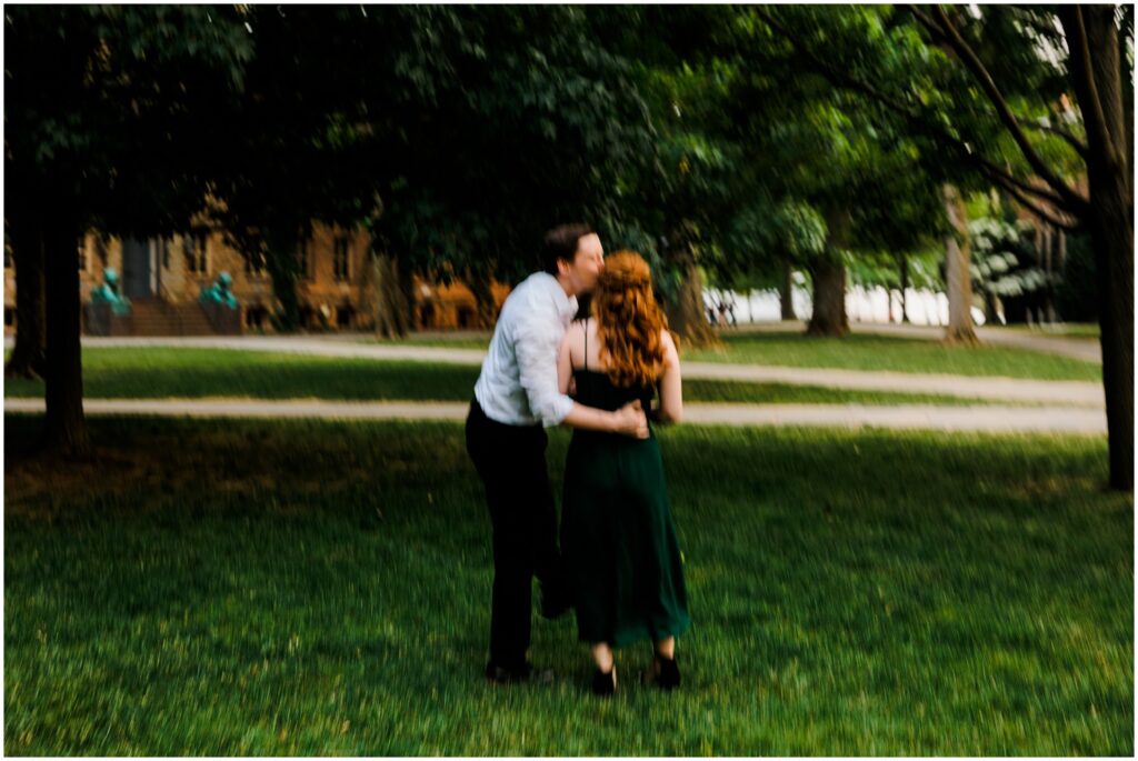 A man kisses a woman's cheek on a lawn in creative engagement photos.