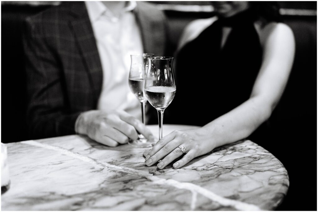 A man and woman set their champagne flutes on a marble bar table.