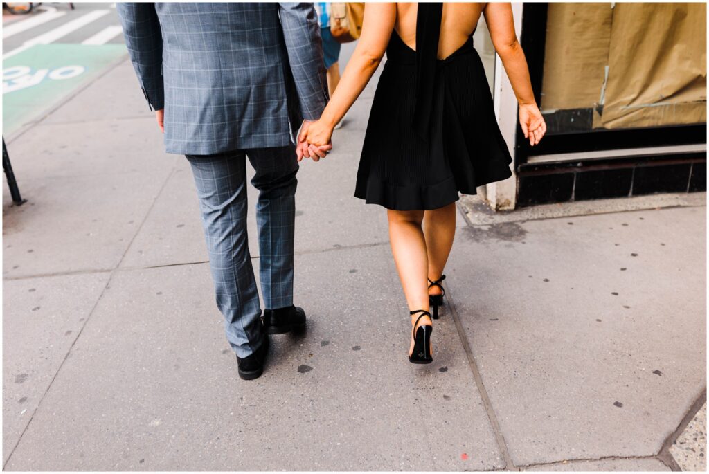 A man and woman hold hands as they walk on a New York City sidewalk.