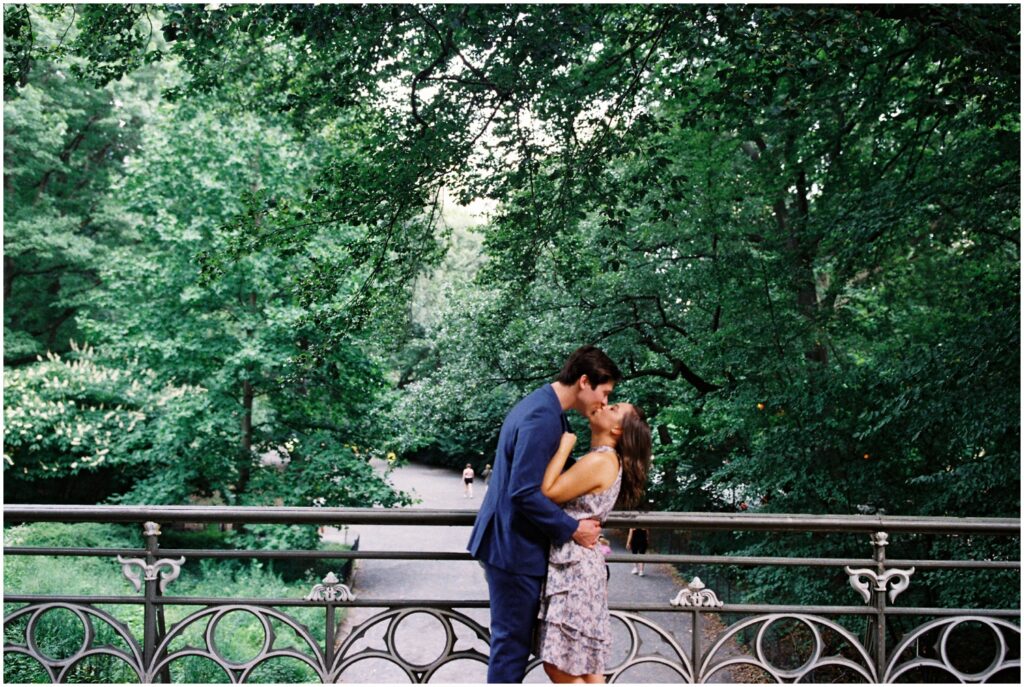 A man and woman kiss on a bridge overlooking Central Park.