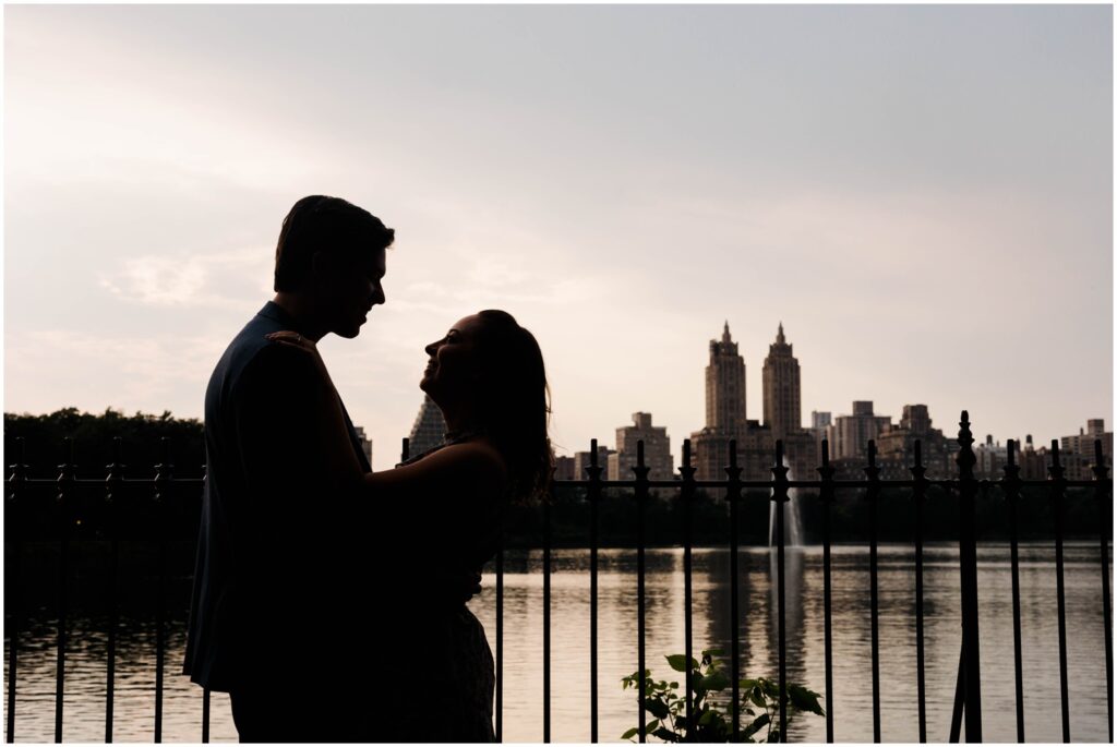 A man and woman are silhouetted against the New York City skyline in an engagement photo.