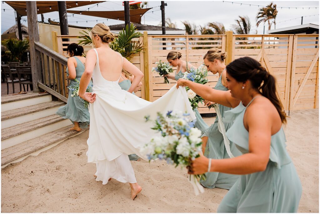 Bridesmaids carry the train of a bride's wedding dress as they run across the sand at a beach wedding in New Jersey.