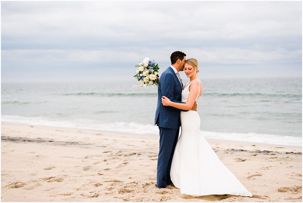 A groom kisses a bride's cheek at their beach wedding in New Jersey.