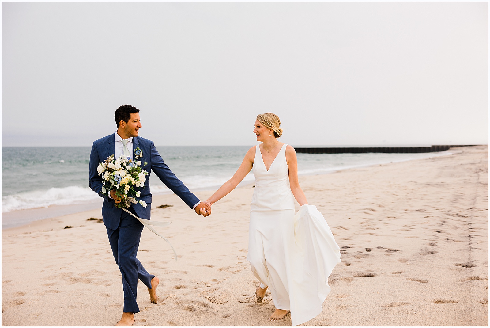 A bride and groom hold hands and run down a beach towards a New Jersey wedding photographer.